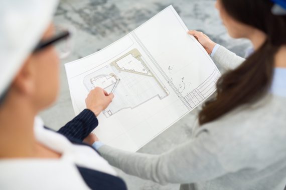 Building designers discussing housing project and viewing blueprint during meeting at construction site