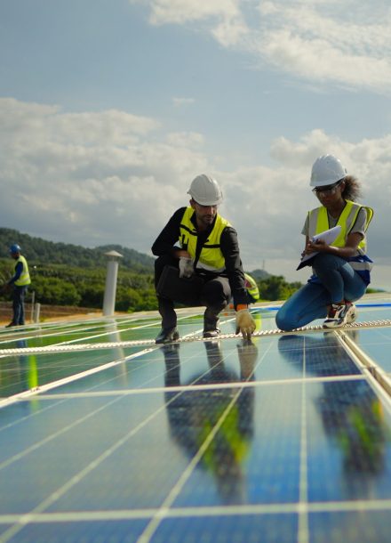 Team contractor, male engineer and female technicians  wearing safety uniform, talking about installing plan, check the working system and maintenance solar panel of solar power plant to produce electricity on the roof of factory building. Industrial of renewable energy. Power generation from solar energy.